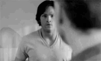 a man in a t-shirt is looking at himself in the mirror .
