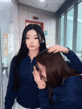 a woman touching another woman 's hair in front of a sign that says ' no smoking ' on it