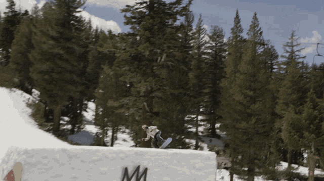 a snowboarder is doing a trick on a snowy slope with trees in the background