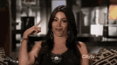 a woman is sitting on a couch making a funny face and pointing her finger up .