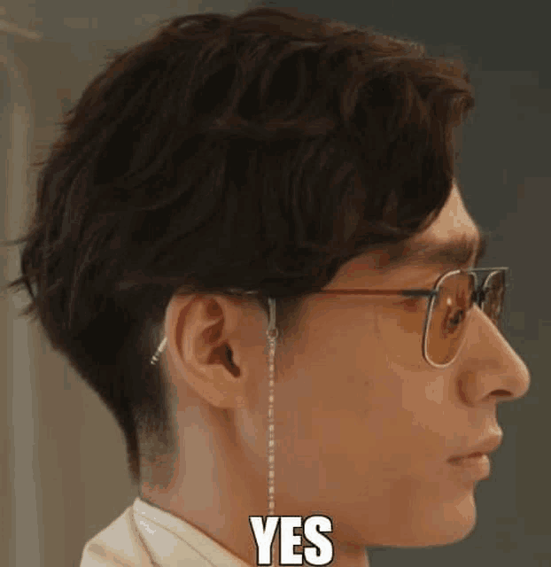 a man wearing sunglasses with a chain around his ear is making a yes sign .