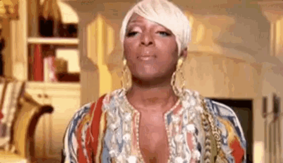a woman is making a funny face in a living room while wearing a colorful shirt and earrings .