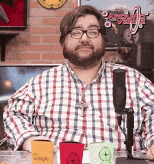 a man wearing glasses and a plaid shirt sitting in front of a microphone