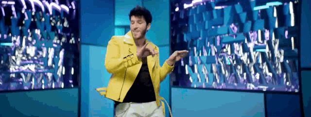 a man wearing a yellow jacket is dancing in front of a large screen