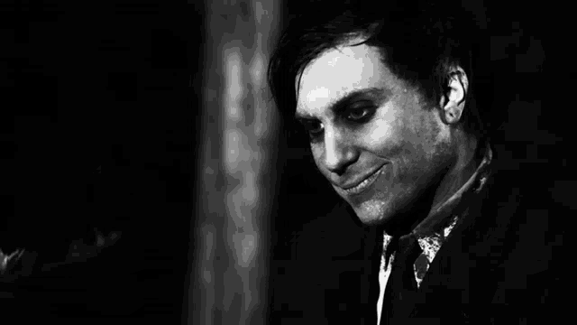 a black and white photo of a man in a suit and tie with black eyes .