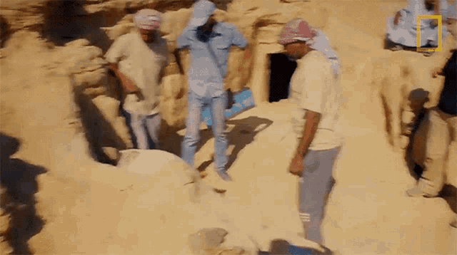 a group of people are standing in a sandy area with a national geographic logo in the corner