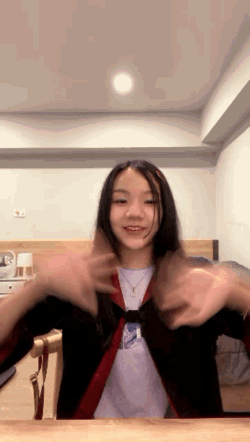 a girl wearing a black cardigan and a purple shirt with the letter a on it is sitting at a table