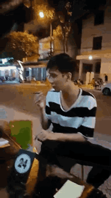 a man in a striped shirt is sitting at a table with a sign that says 24 on it .