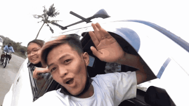 a man in a white shirt is waving his hand out of the window