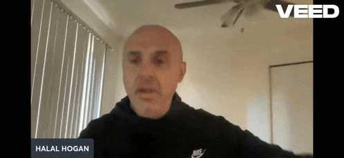 a bald man wearing a black nike shirt is talking on a video call with the name halal hogan on the screen