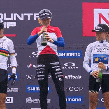 a woman is holding a bottle of wine in front of a banner that says shimano on it
