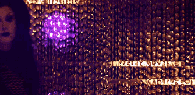 a woman stands in front of a wall of skulls with a purple light in the middle