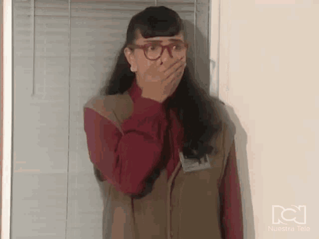a woman in glasses is covering her mouth with her hand .