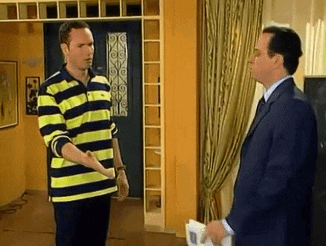a man in a striped shirt and a man in a suit are standing next to each other in a room .