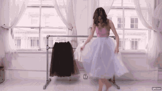 a woman in a pink top and purple skirt is standing in front of a window ..