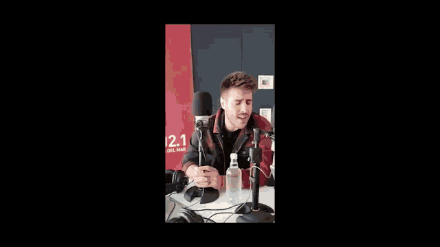 a man is sitting in front of a microphone with a bottle of water next to him .