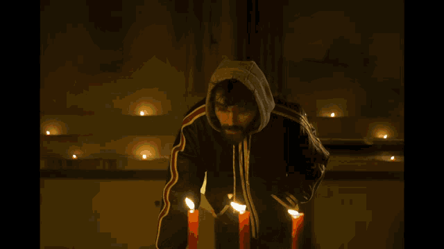 a man in a hooded jacket is lighting candles in the dark