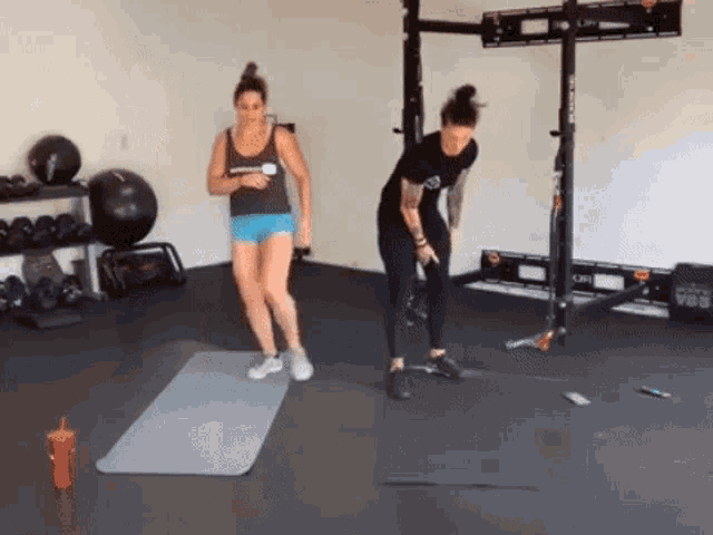 two women are doing exercises in a gym while standing on a mat .