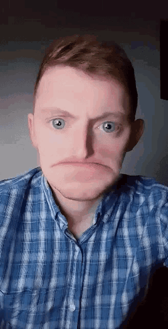 a man wearing a blue plaid shirt is making a funny face