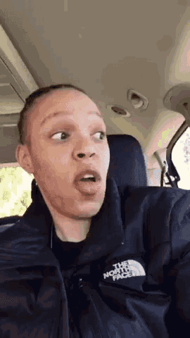 a woman in a north face jacket is making a funny face while sitting in a car .