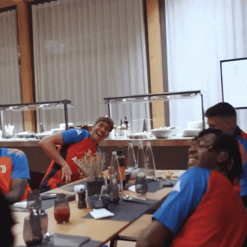 a man wearing a red shirt that says ' allianz ' on it sits at a table