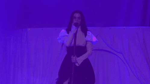a woman singing into a microphone in front of a blue curtain