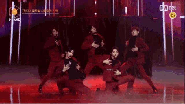 a group of men in red suits are dancing on a stage in front of a mnet sign