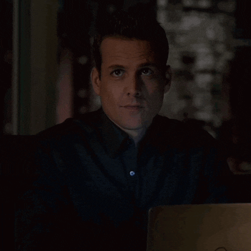 a man in a black shirt is sitting in front of a laptop and smiling .