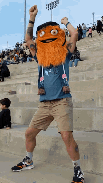 a man in a mascot costume stands on a set of bleachers with his fist in the air