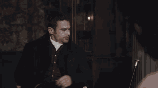 a man in a tuxedo is standing in a dark room with candles .