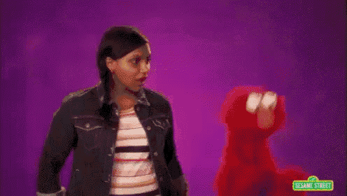 a woman is dancing with elmo from sesame street while holding a ball .