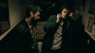 two men are talking in a bathroom with posters on the wall including one that says ' i 'm not a fan '