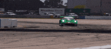 a green race car is driving down a track with a weathertech sign in the background