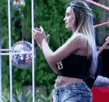 a woman in a black crop top and shorts is standing in front of a disco ball in a cage .