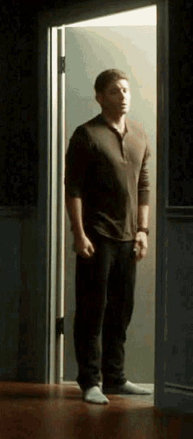 a man in a brown shirt and black pants stands in an open doorway