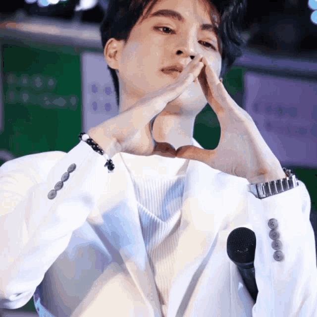 a man in a white suit is making a heart with his hands