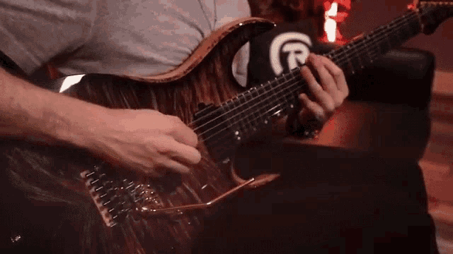 a man is playing a guitar with the letter r on the back of his shirt