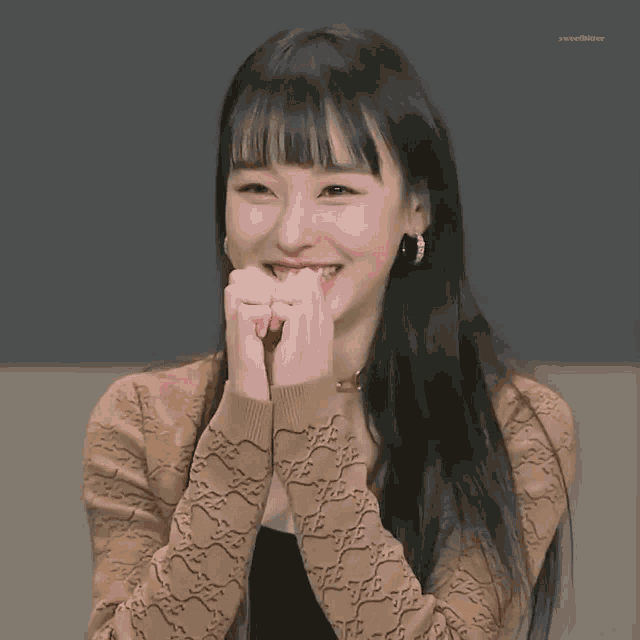 a woman with long hair and bangs is smiling with her hands covering her mouth