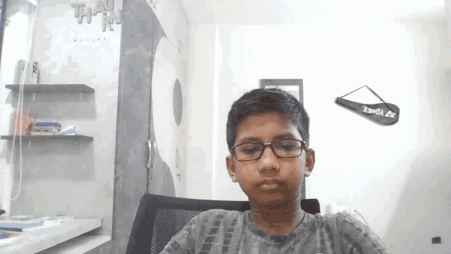 a young boy wearing glasses is sitting in front of a wall that says " thank you "