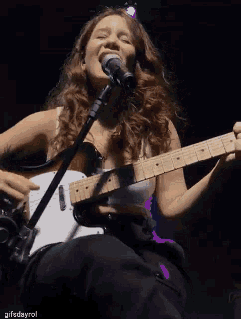 a woman singing into a microphone while holding a guitar in front of her