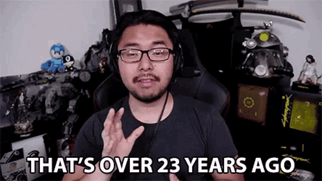 a man wearing glasses and headphones says that 's over 23 years ago while sitting in a gaming chair .