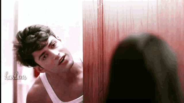 a man in a white tank top looks at his reflection in a mirror