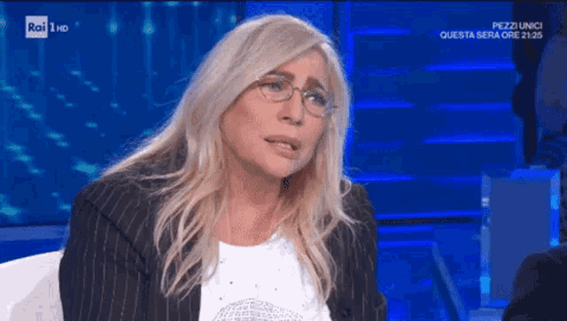 a woman wearing glasses and a striped jacket is sitting on a couch on a rai tv show