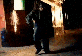 a man in a black coat is dancing on the sidewalk in front of a building .