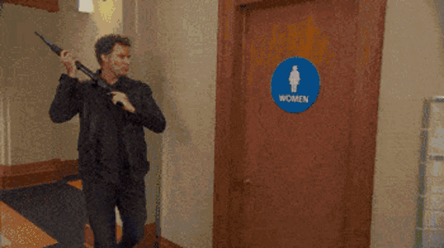 a man holds a gun in front of a women 's restroom