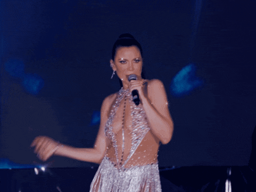 a woman in a very revealing silver dress sings into a microphone