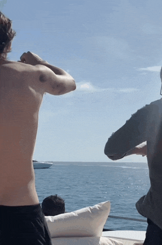 a man without a shirt is standing on a boat looking at the ocean