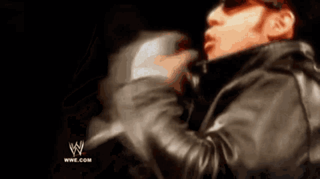 a man in a leather jacket is holding a microphone in front of a wrestling logo .