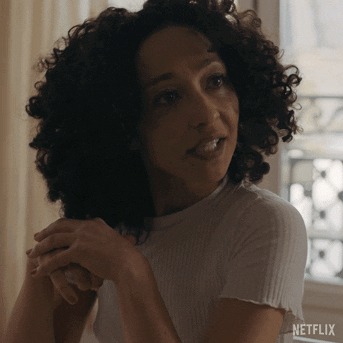 a woman with curly hair is sitting in front of a window with netflix written on the bottom