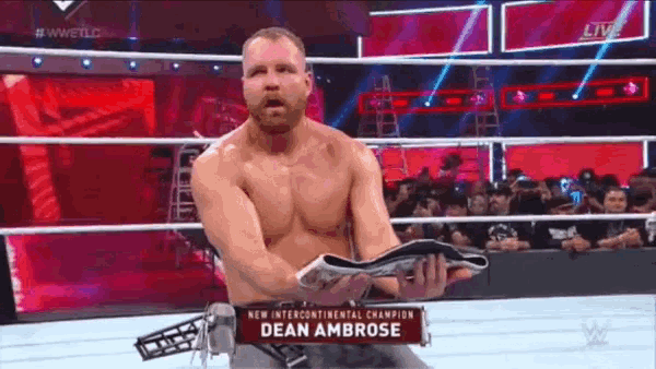 a shirtless wrestler is holding a championship belt in a wrestling ring .